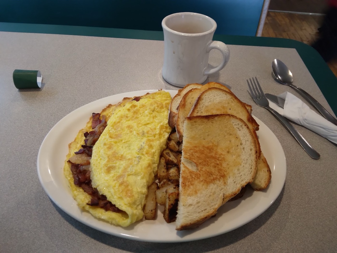 A folded cheese omelet with home fries, toast and a mug of coffee on a diner table.