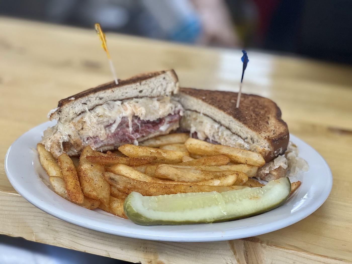 A Reuben sandwich on grilled rye with seasoned fries and a dill pickle spear.